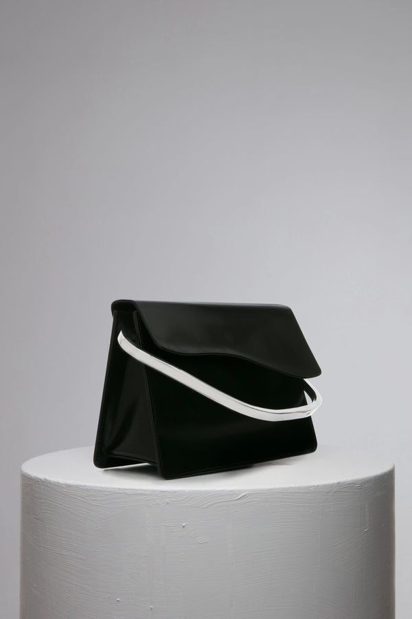 rectangular black leather handbag with metal top handle on white stand