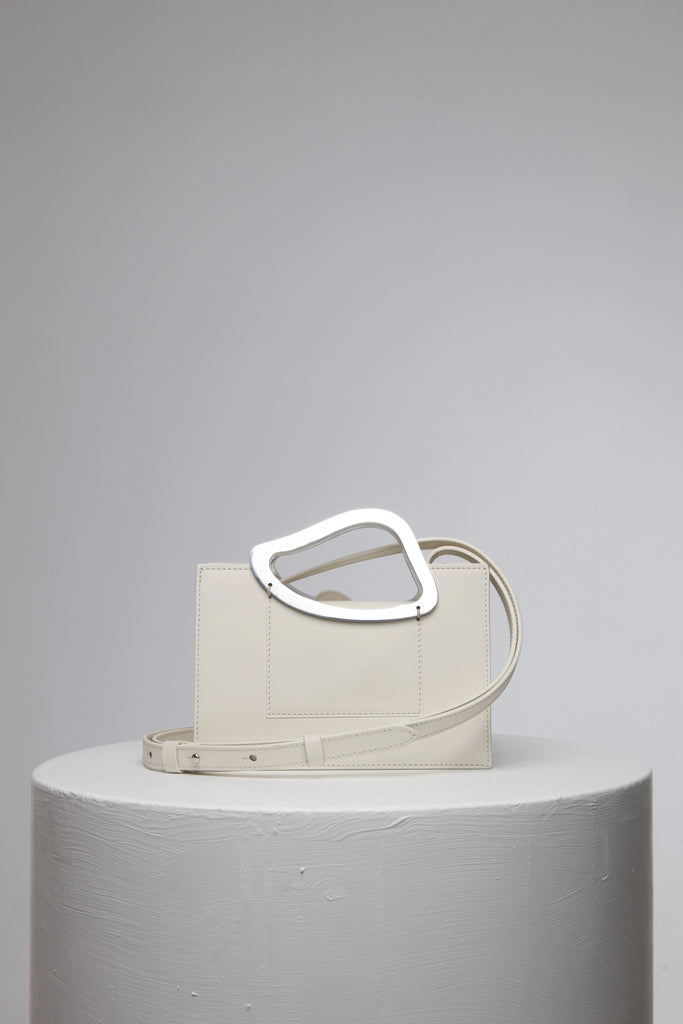 rectangular white geunine leather handbag with metal top handle on white stand
