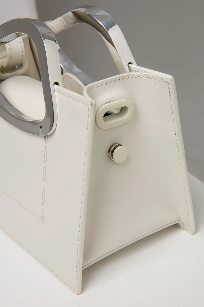 rectangular white geunine leather handbag with metal top handle on white stand